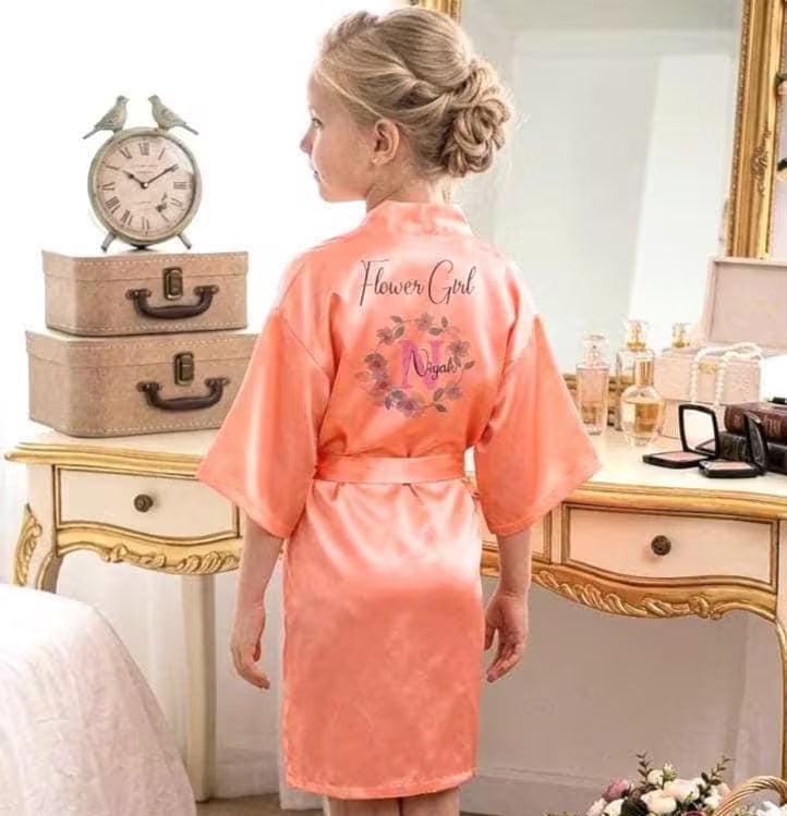 Woman wearing a pink 'Flower Girl Night' robe in a bedroom setting.