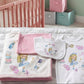 A coordinated baby bedding set displayed on a bed in a nursery, including a folded blanket, a bib, and a baby top. The set features Alice in Wonderland illustrations, a pink accent piece, and the name 'Mellie' printed on the top.