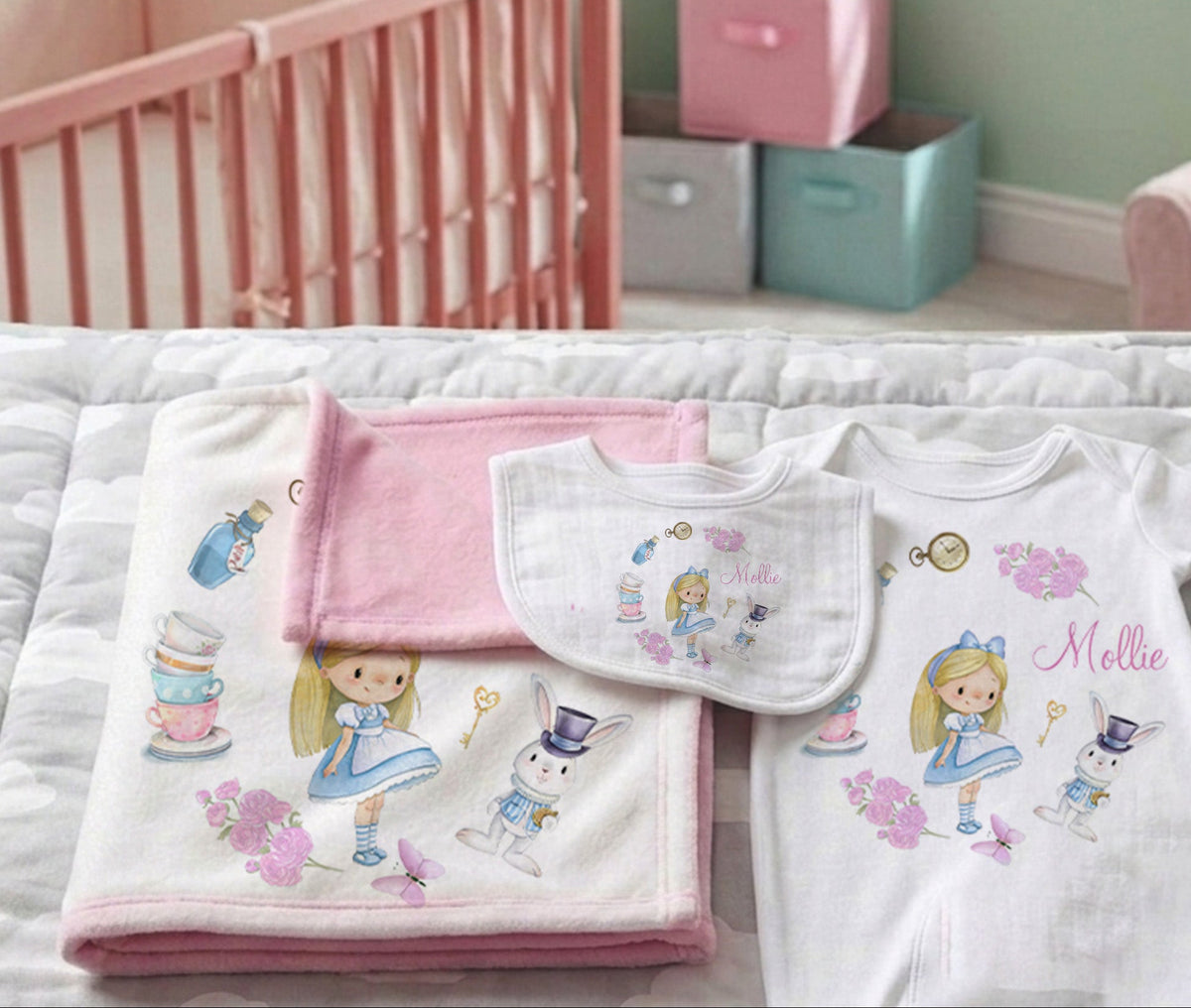 A coordinated baby bedding set displayed on a bed in a nursery, including a folded blanket, a bib, and a baby top. The set features Alice in Wonderland illustrations, a pink accent piece, and the name 'Mellie' printed on the top.