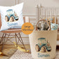 Personalized nursery decor set featuring a white throw pillow and a beige fabric storage bin, both printed with a blue tractor illustration and the name 'Simon'. The scene is styled in a nursery with a rocking chair, crib, and toys.