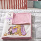 A personalized baby blanket featuring Winnie the Pooh and a duckling, folded on a gray cloud-patterned quilt in a nursery setting with a pink crib in the background.