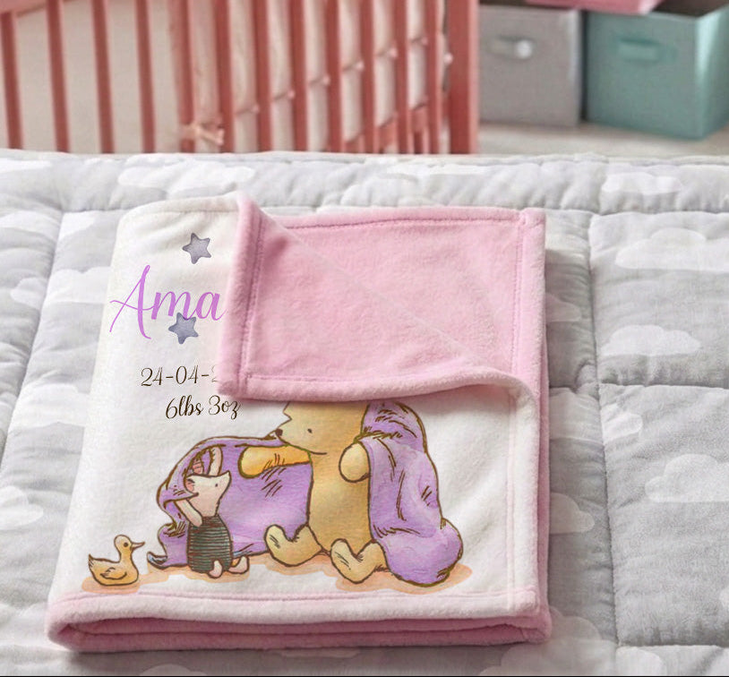 A personalized baby blanket featuring Winnie the Pooh and a duckling, folded on a gray cloud-patterned quilt in a nursery setting with a pink crib in the background.
