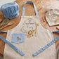 Personalized kids safari chef set with blue trim apron, matching blue chef hat, and drawstring bag featuring watercolor lion and giraffe illustrations on a kitchen counter.