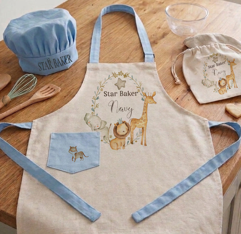Personalized kids safari chef set with blue trim apron, matching blue chef hat, and drawstring bag featuring watercolor lion and giraffe illustrations on a kitchen counter.
