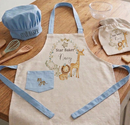 Personalized kids safari chef set with blue trim apron, matching blue chef hat, and drawstring bag featuring watercolor lion and giraffe illustrations on a kitchen counter.