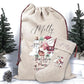 A personalized Christmas gift sack and matching stocking set in natural burlap, printed with the name Molly, a snowman, Santa, and the phrase 'Believe in the Magic of Christmas.' The set is styled with small artificial Christmas trees and pinecones on a white surface against a white background.