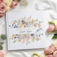 Greeting card with floral design and text on a marble surface with flowers and ribbon.
