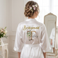 Woman wearing a white satin robe with 'Bridesmaid Tiffany' printed on it in a room.