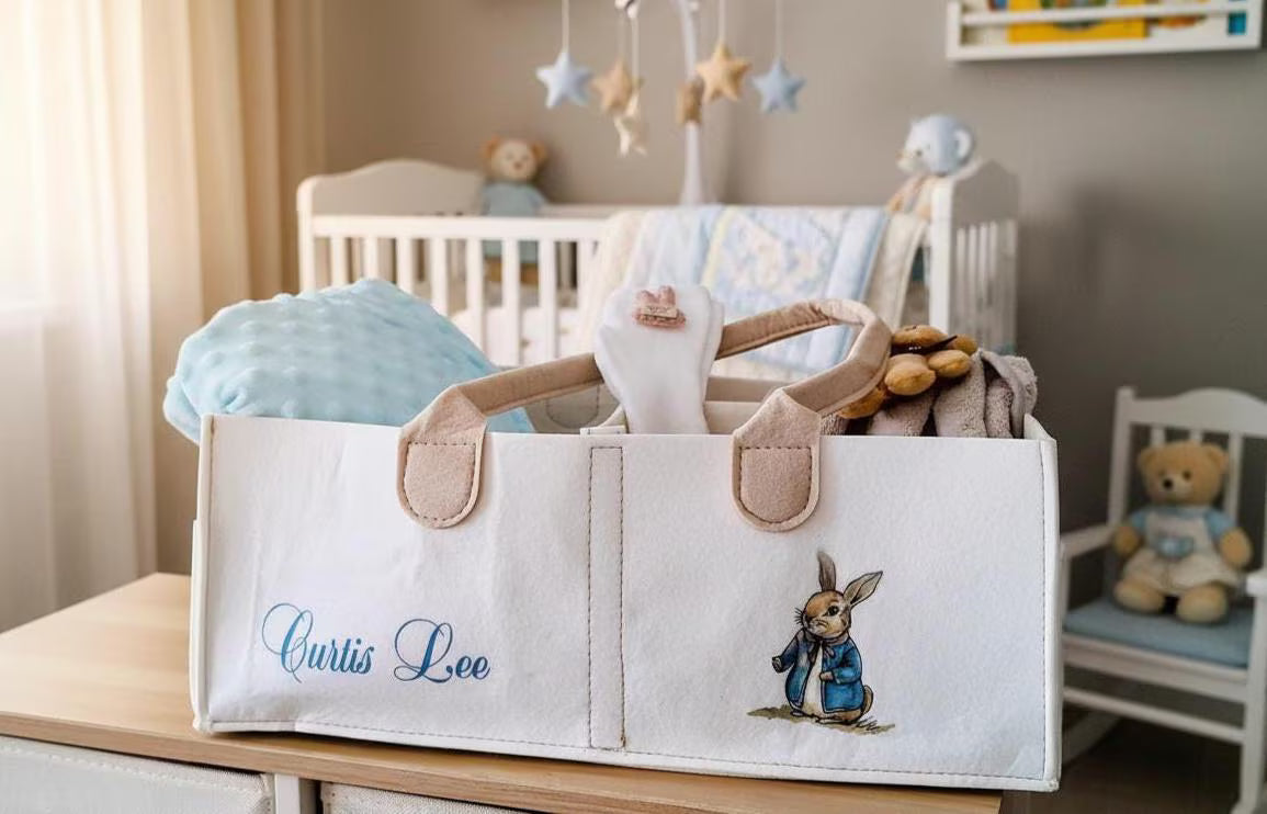 A personalized canvas baby storage tote bag with Beatrix Potter bunny illustration and the name 'Curtis Lee' embroidered in blue, filled with baby items in a nursery setting.