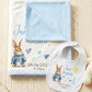 Personalized baby blanket and bib set featuring Peter Rabbit illustration and the name 'Jan Smith' with birth date and time, styled with a teddy bear on a cream cable-knit blanket.