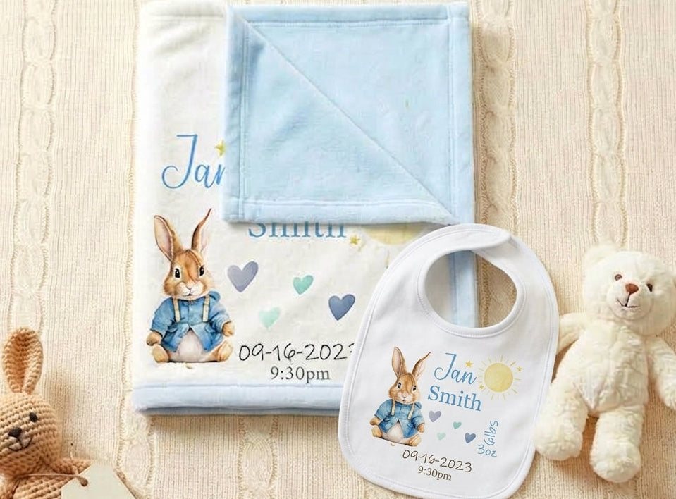 Personalized baby blanket and bib set featuring Peter Rabbit illustration and the name 'Jan Smith' with birth date and time, styled with a teddy bear on a cream cable-knit blanket.