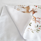 A white waffle-weave kitchen towel with a watercolor design of two deer and a leafy wreath, shown on a light gray marble surface.