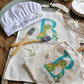 Personalized kids dinosaur baking set with custom name chef hat and apron on a wooden kitchen table with baking supplies.