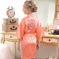 Woman wearing a pink 'Flower Girl Night' robe in a bedroom setting.