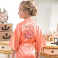 Woman wearing a pink 'Flower Girl Night' robe in a bedroom setting.