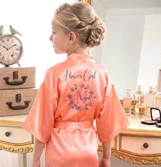Woman wearing a pink 'Flower Girl Night' robe in a bedroom setting.