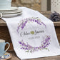 Ceramic cups and saucers with a personalized towel featuring a floral design and text on a wooden surface.