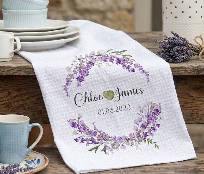 Ceramic cups and saucers with a personalized towel featuring a floral design and text on a wooden surface.