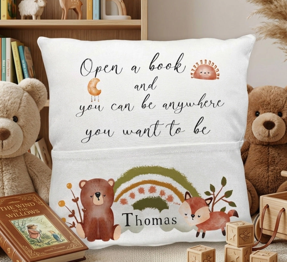 A personalized white throw pillow featuring a woodland theme with the quote 'Open a book and you can be anywhere you want to be' and the name 'Thomas'. The pillow is decorated with illustrations of a brown bear, a fox, a small hedgehog, a rainbow, and leaves.