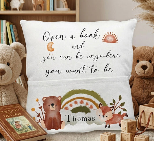 A personalized white throw pillow featuring a woodland theme with the quote 'Open a book and you can be anywhere you want to be' and the name 'Thomas'. The pillow is decorated with illustrations of a brown bear, a fox, a small hedgehog, a rainbow, and leaves.