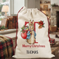 A personalized Christmas Santa sack featuring a cartoon illustration of Thomas the Rabbit, with 'Merry Christmas' and the name 'THOMAS' printed on it. The sack is set in a cozy, decorated living room environment.