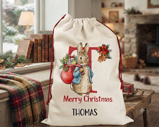 A personalized Christmas Santa sack featuring a cartoon illustration of Thomas the Rabbit, with 'Merry Christmas' and the name 'THOMAS' printed on it. The sack is set in a cozy, decorated living room environment.
