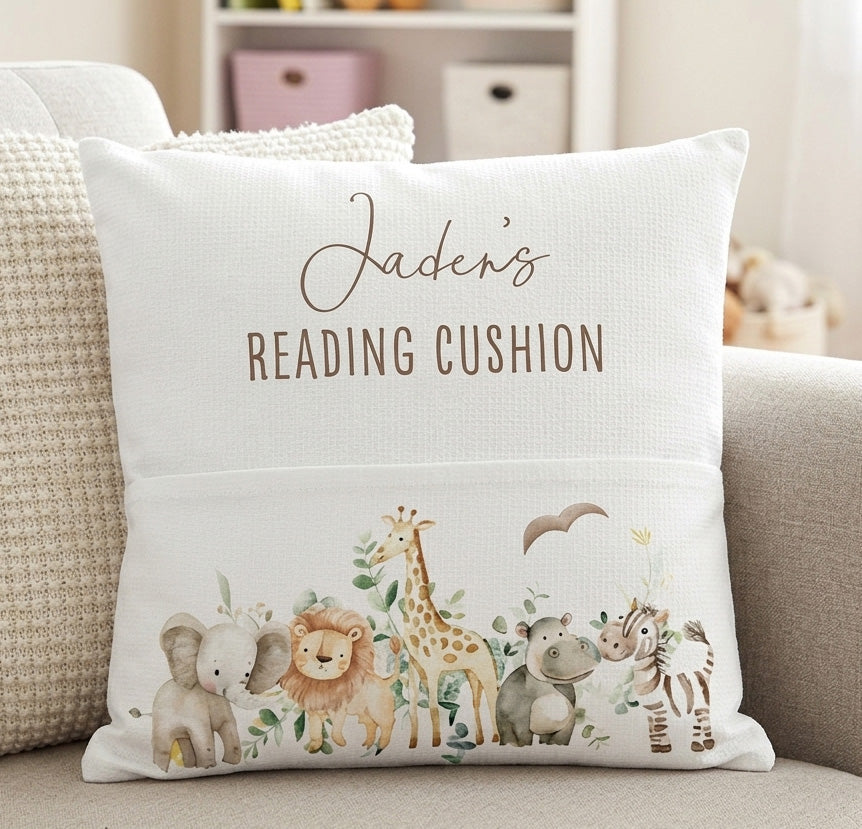 A personalized white throw pillow with a watercolor safari animal design and the text 'Jaden's READING CUSHION', displayed on a beige sofa.