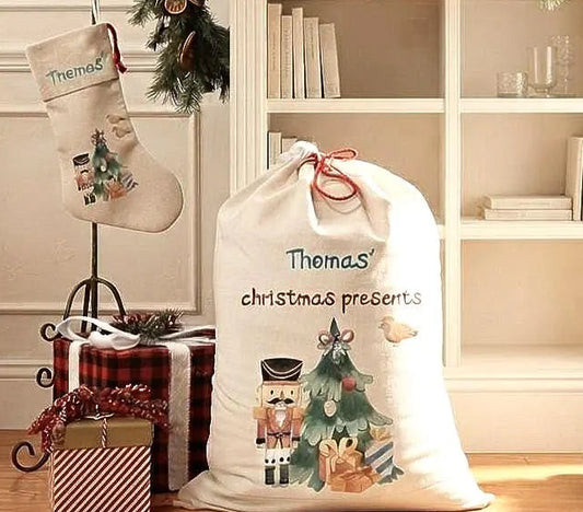 A personalized cream-colored Christmas Santa sack with 'Thomas' and 'Christmas presents' printed on it, styled in a cozy holiday room next to a matching hanging stocking.