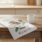 Kitchen towel with a bird design and 'Rosie' text on a wooden surface with a mug.