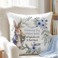 A personalized square white pillow featuring a watercolor illustration of Peter Rabbit in a blue jacket holding a yellow rose, surrounded by blue flowers and green leaves. The text reads 'On your Christening Day William Smith 1st September 2024 St.