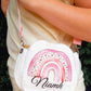 A person wearing a cream top and white skirt carries a small white crossbody bag with a pink watercolor rainbow design and the name 'Niamh' in black script.