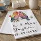 Personalized kitchen towel with colorful birds and text on a wooden table with mugs.