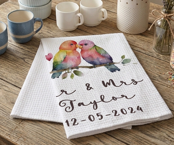 Personalized kitchen towel with colorful birds and text on a wooden table with mugs.